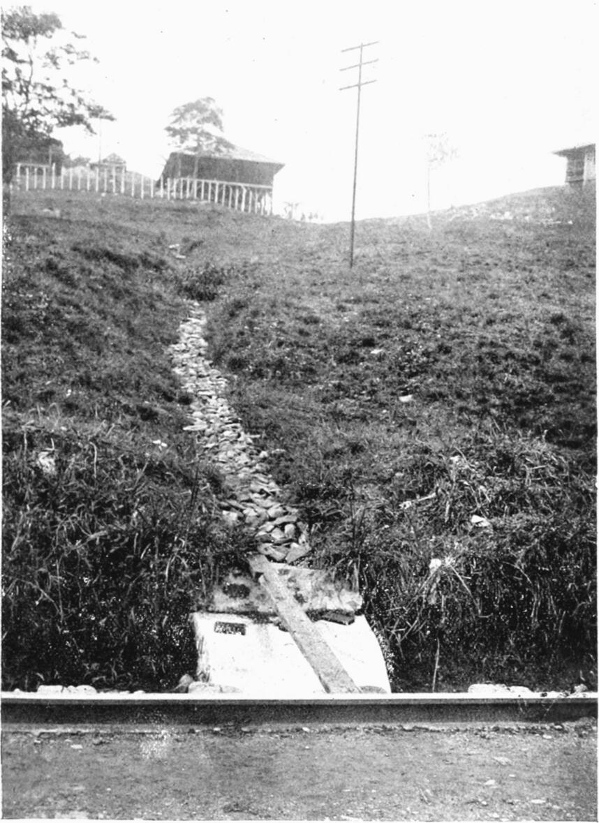 Photograph of a stone-covered subsoil drainage running downhill and
                opening into a trench shown in the foreground